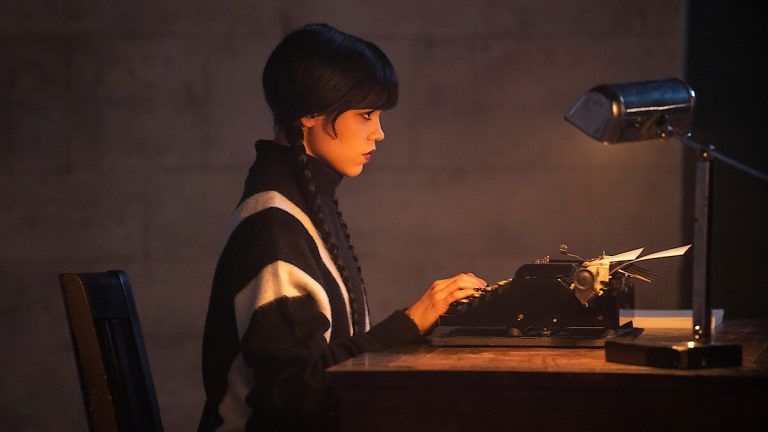 Jenna Ortega as Wednesday Addams writing at a typewriter in Wednesday Season 3